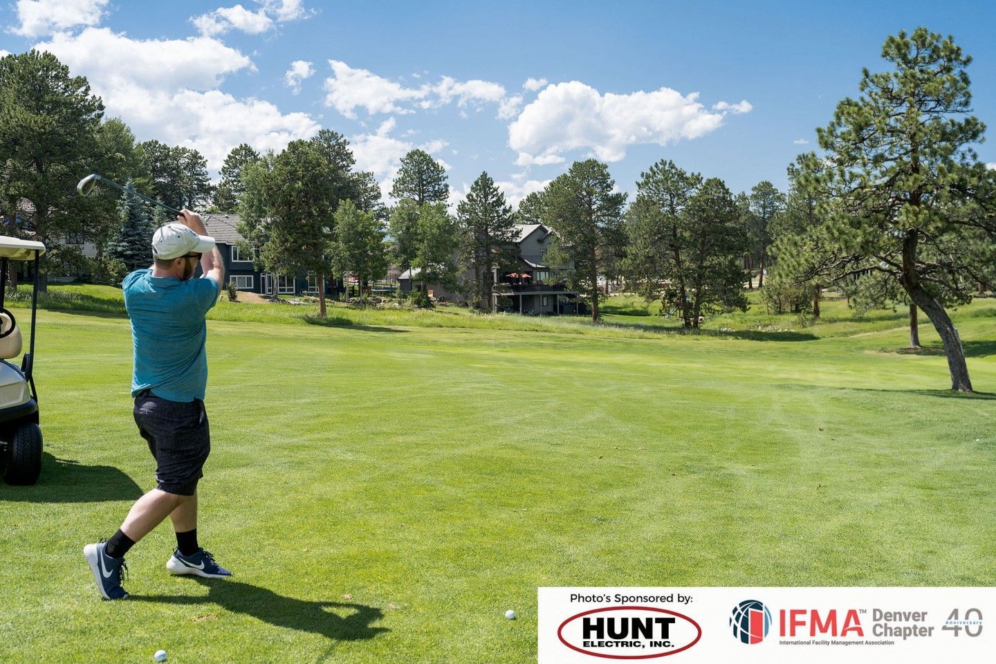 Man in teal shirt swings golf club on green course.