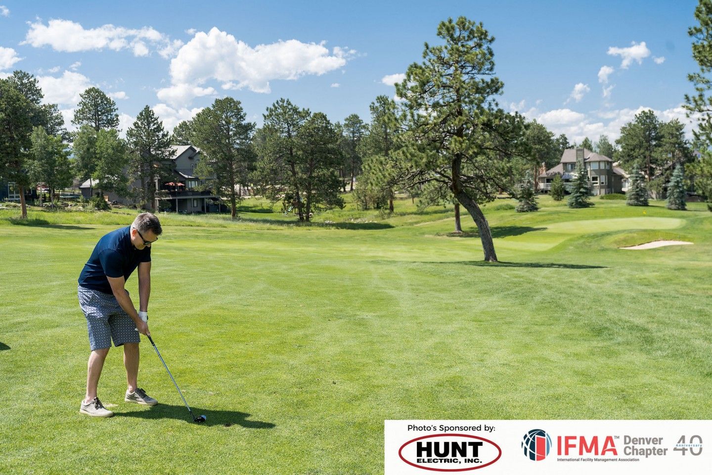 Man swinging a golf club on a green course under a blue sky.