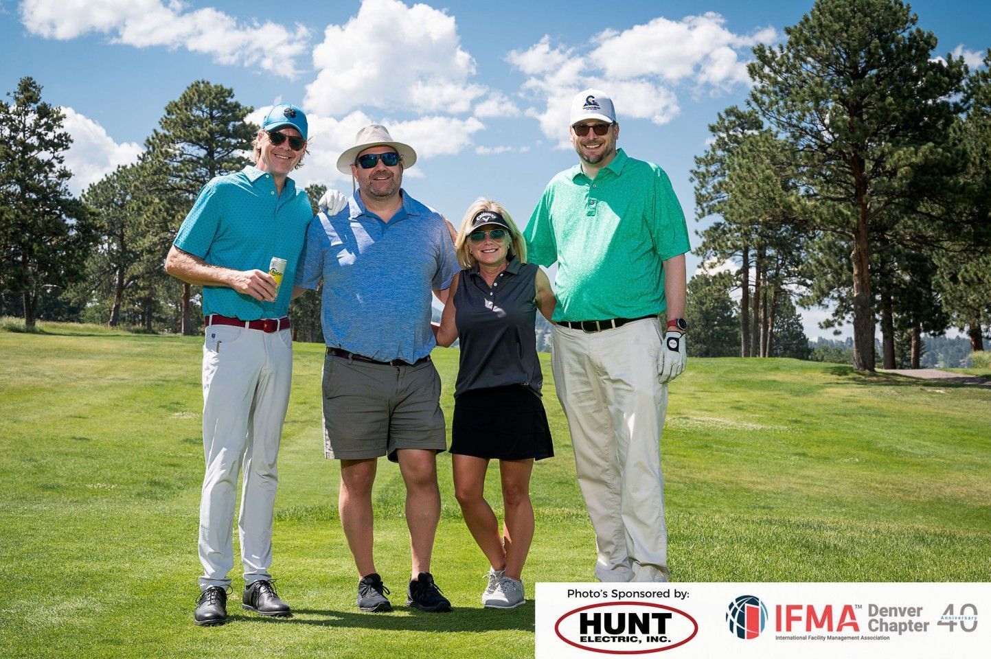 Four people on a golf course. They are smiling and posing for a photo on a sunny day.