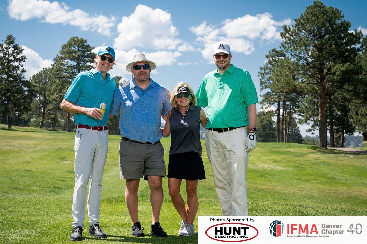 Four people in golf attire on a green. Two men are wearing hats and standing close to a woman in a black skirt.