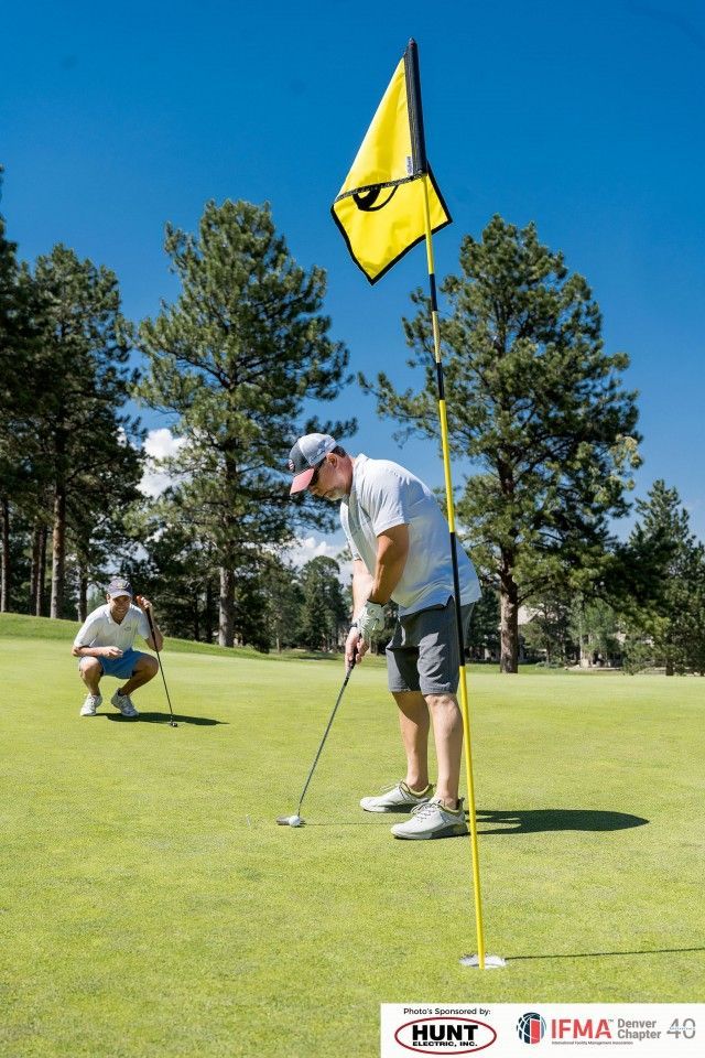 Two golfers putting on a green, yellow flag in the hole, sunny day.