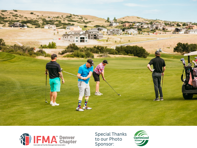 Golfers on a green, preparing to swing. Houses and hills in the background. Golf cart on the right.