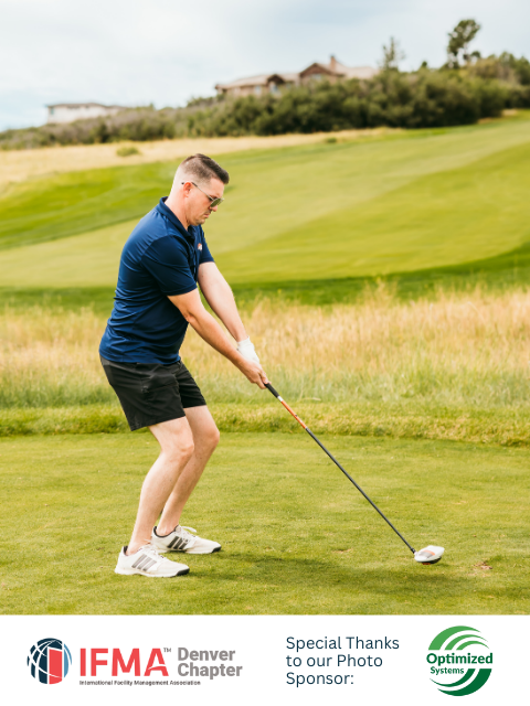 Man tees off on a golf course, wearing blue shirt and black shorts.