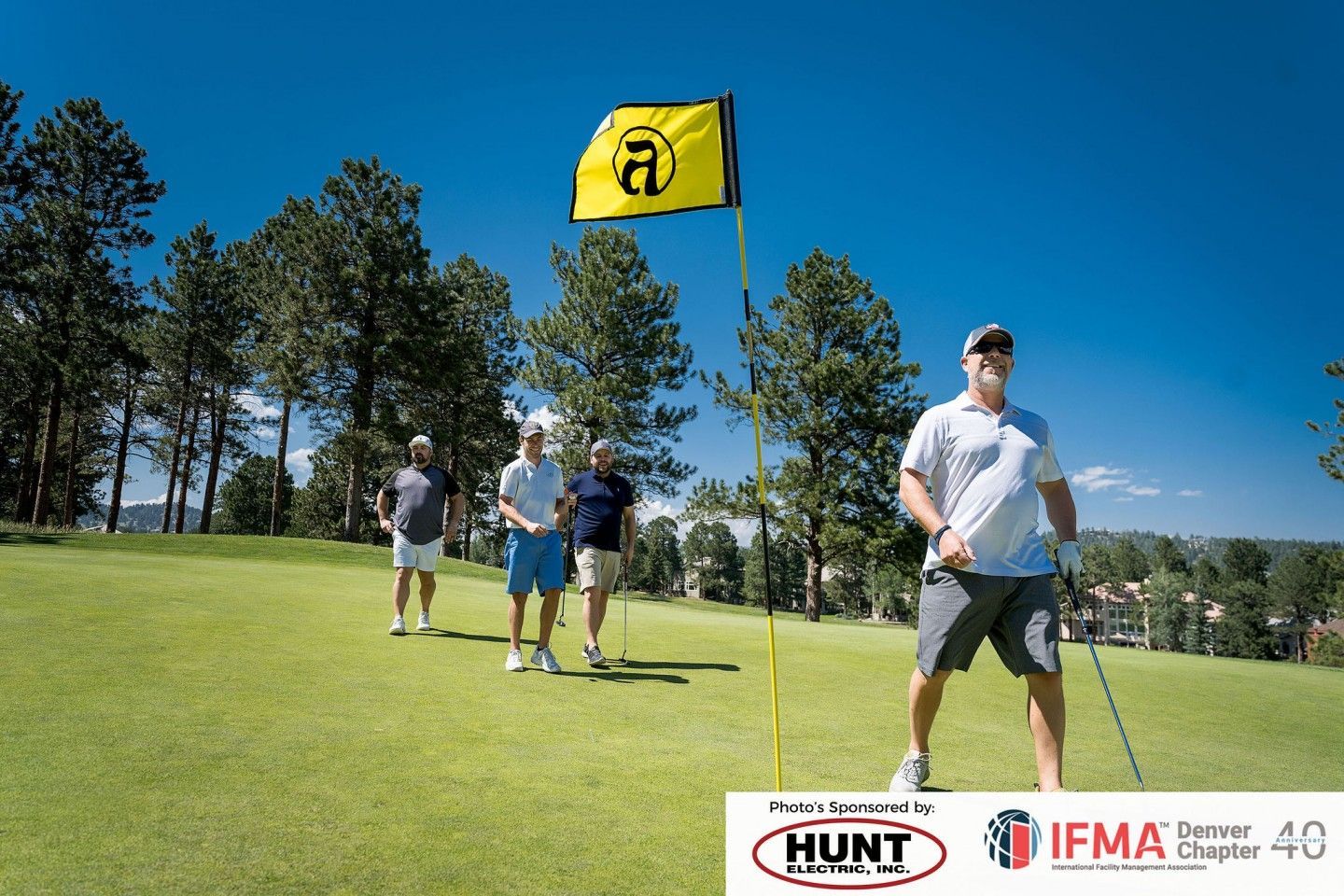 Men golfing on a green, one holding a club, flag in the background, sunny day.