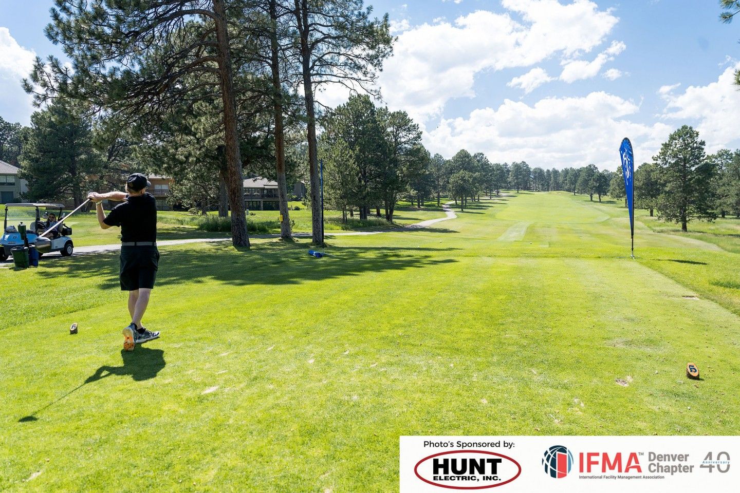 Golfer teeing off on a green golf course under a blue sky, sponsored by Hunt and IFMA.