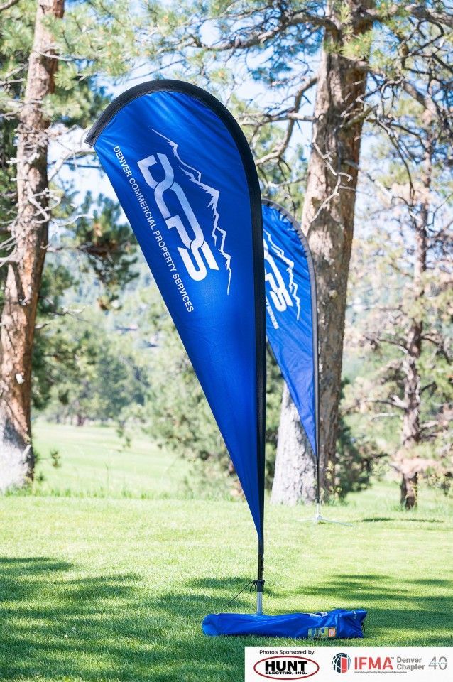Blue teardrop flags with white logo on green grass, trees in background.