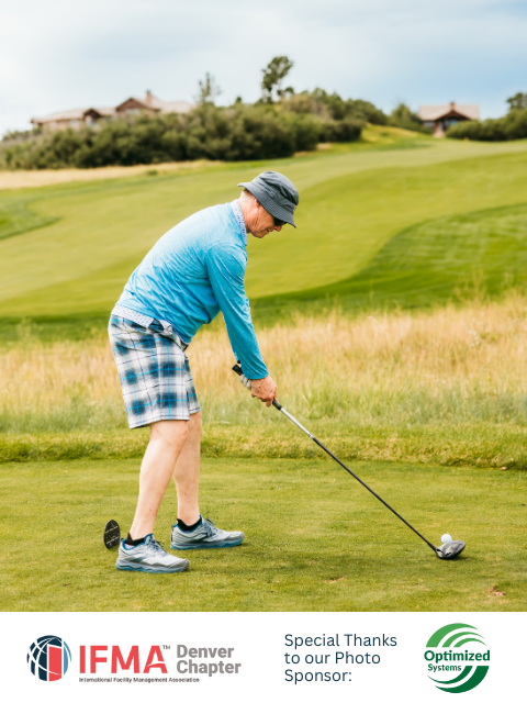 Man in blue shirt and plaid shorts tees off on a golf course.