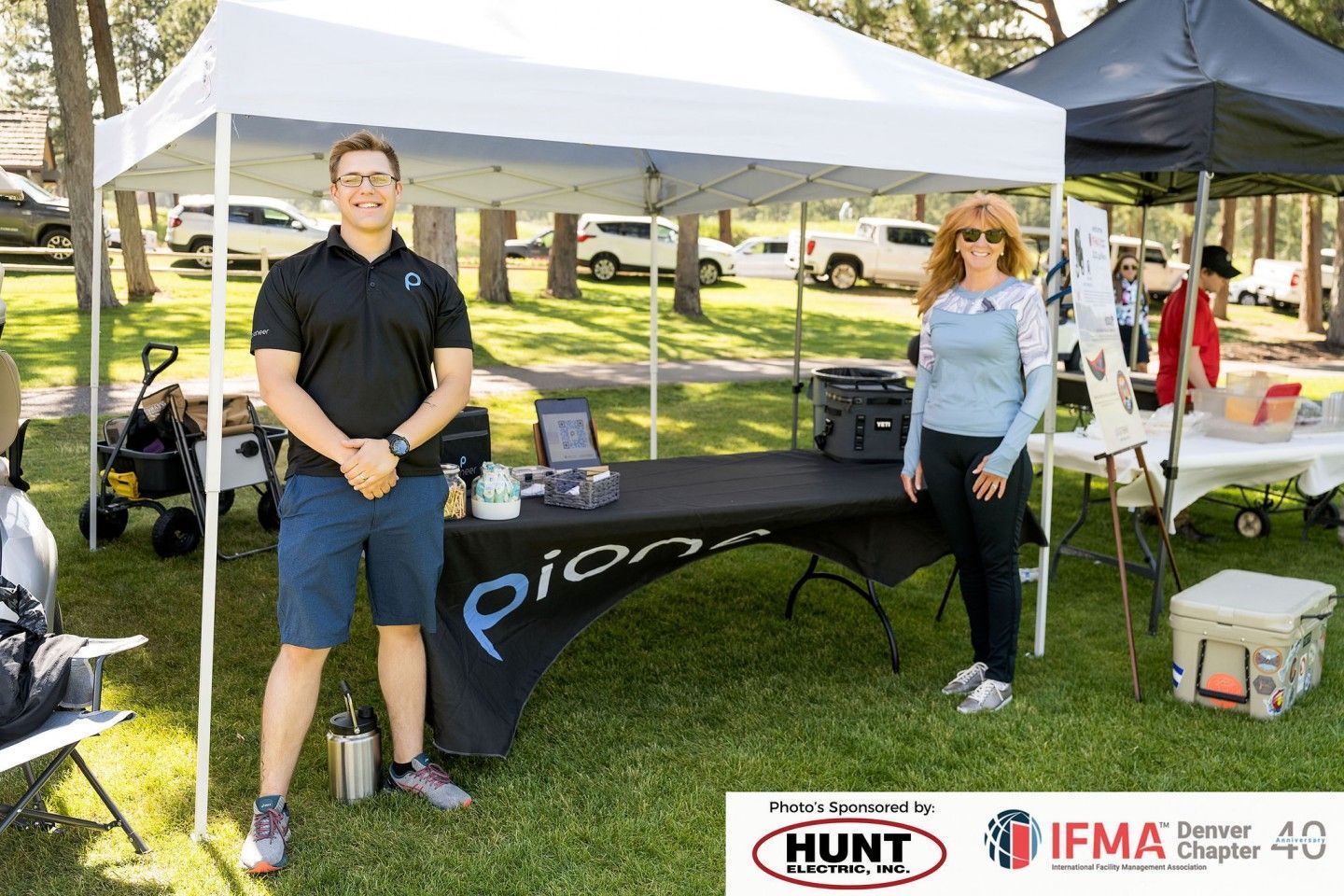 Two people stand at a booth under a canopy, “pionair” logo on the table. Outdoors, sunny.