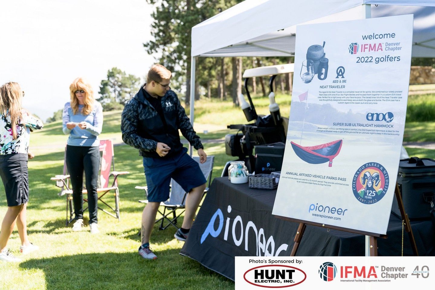 People at an outdoor event with a sign, golf cart, and branding.