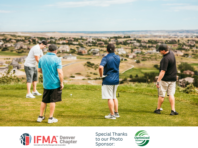 Four men golfing on a green with a scenic view of houses and a city on the horizon.