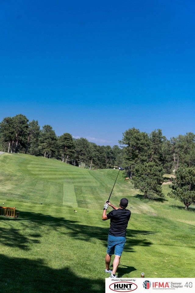 Golfer swings club on a sunny golf course, preparing to hit the ball.