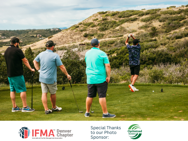 Four men playing golf on a green course, one teeing off, mountain backdrop.