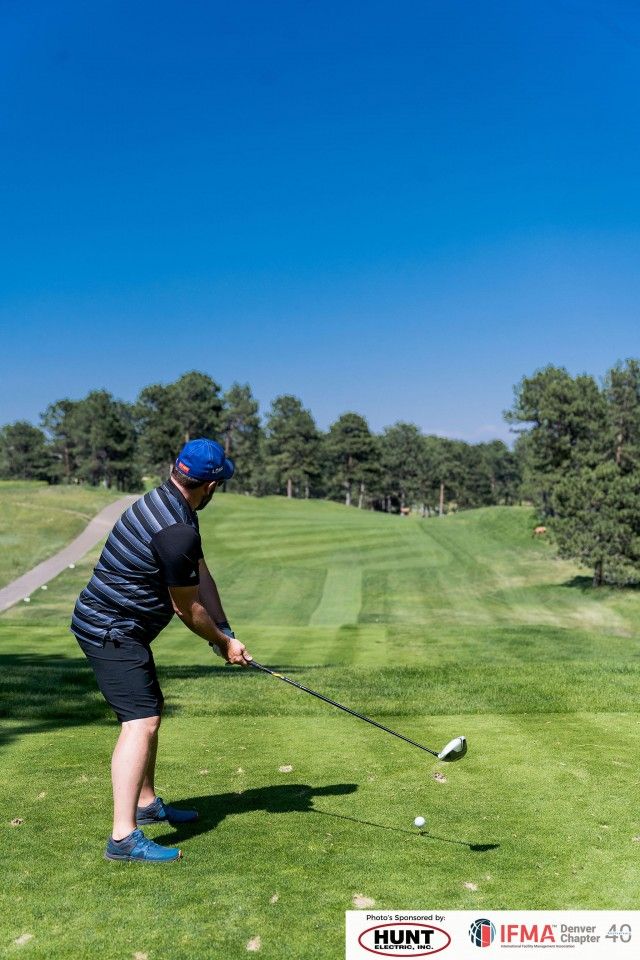 Golfer teeing off on a green golf course under a clear blue sky.