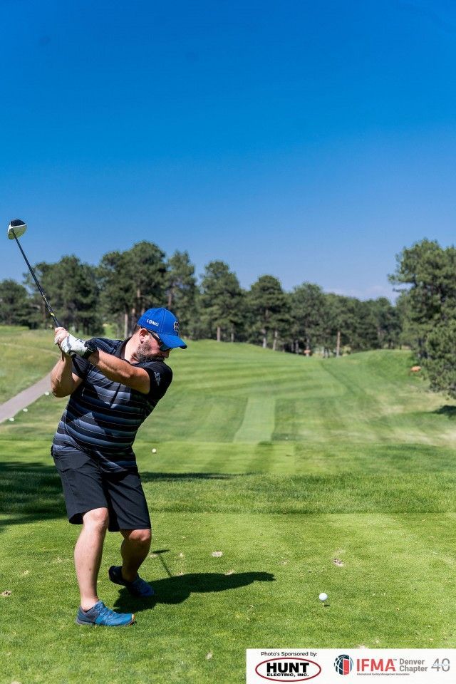 Golfer swings club on green course under a blue sky.