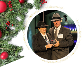 Two people in fedoras and suits holding an award, framed by a Christmas wreath.