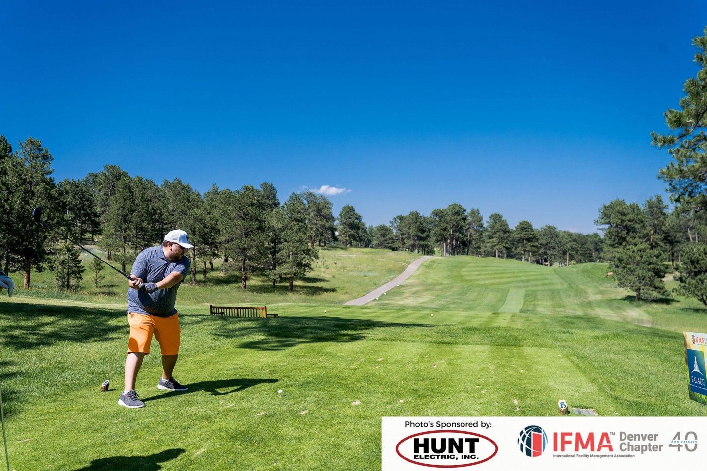 Man in orange shorts swings a golf club on a sunny green golf course.