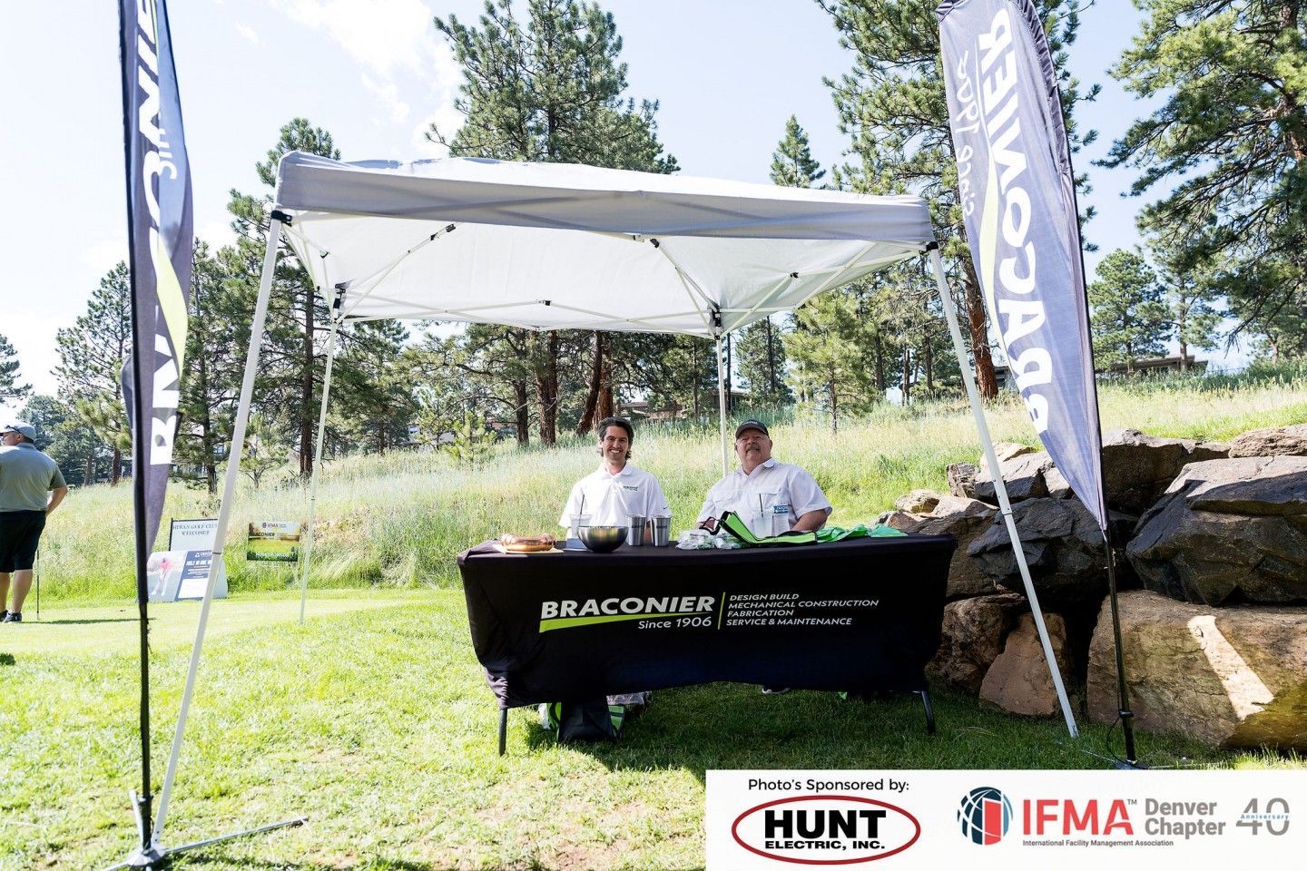 Two people at a vendor table under a canopy at an outdoor event.