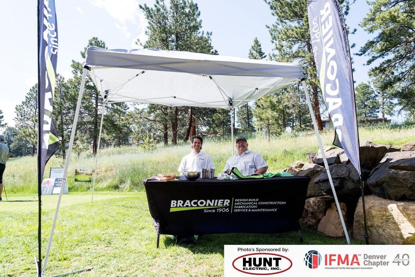 Two chefs at a Braconier food booth under a tent, outside on a sunny day.