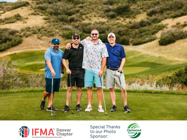 Four men posing with golf clubs on a green, smiling. Mountainous background, sunny day.