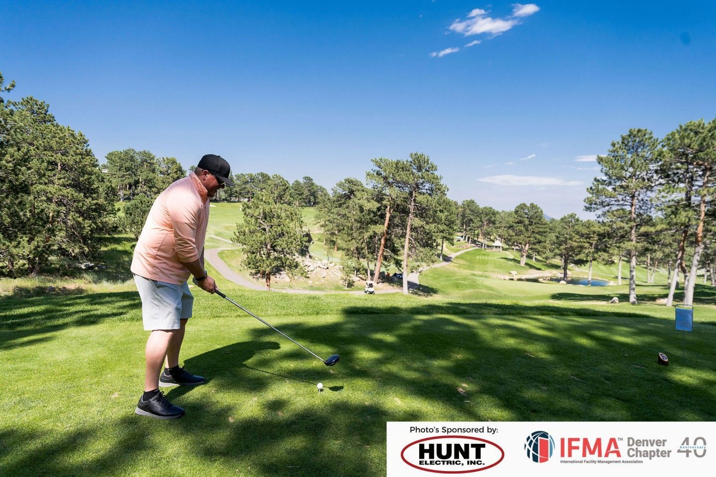 Golfer teeing off on a sunny golf course, wearing a light pink shirt and shorts.