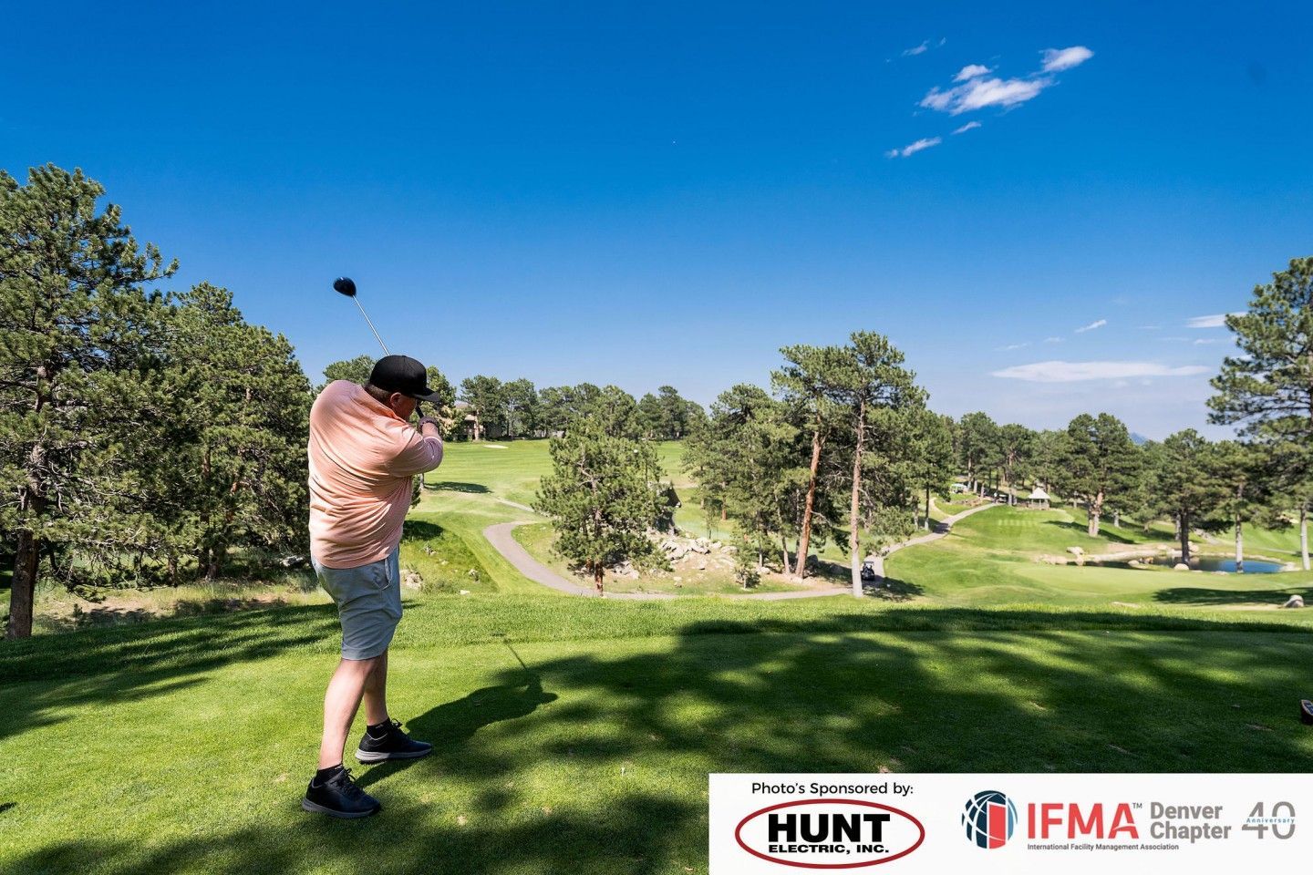 Man swings a golf club on a sunny day at a golf course.