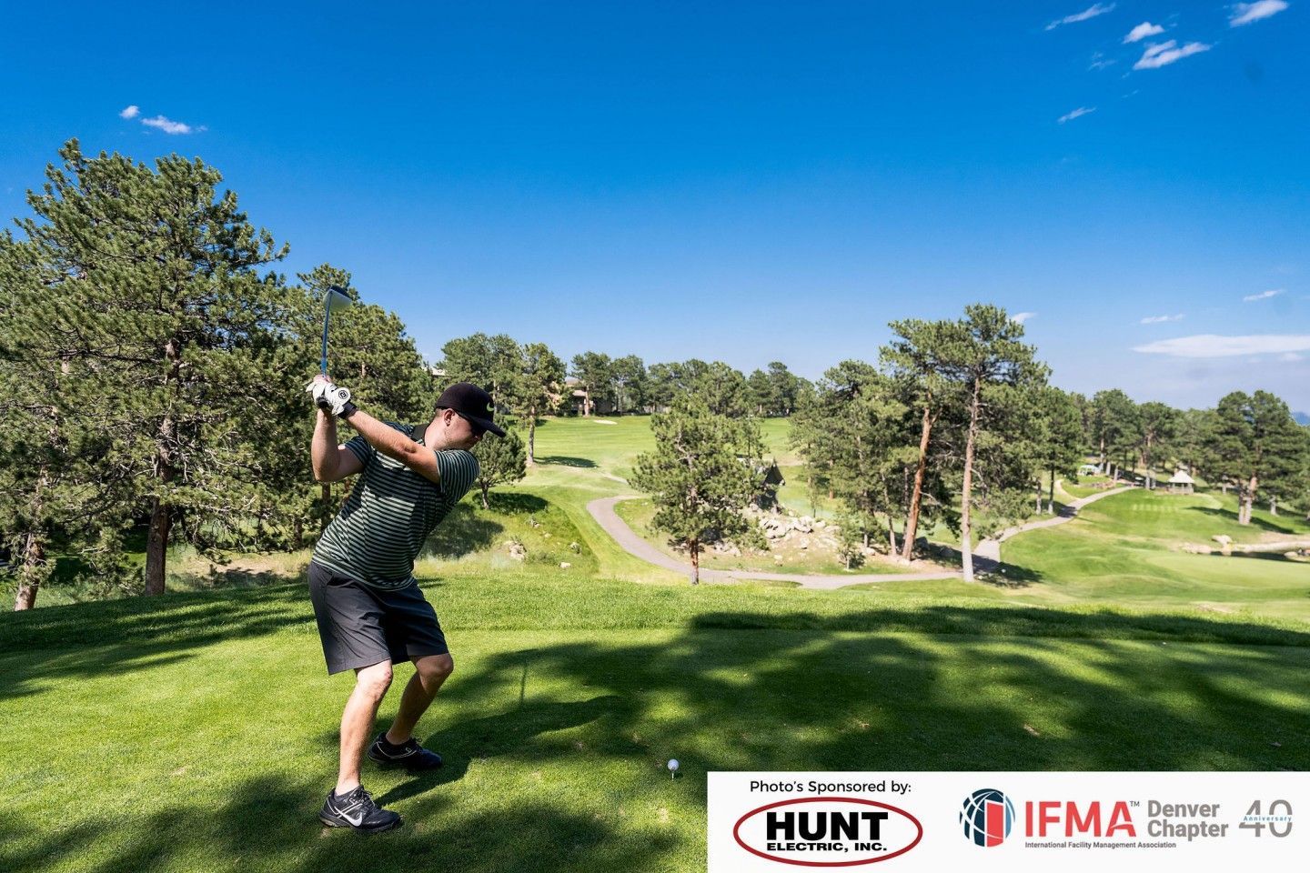 Golfer in green shirt swings at ball on golf course under blue sky.
