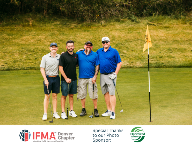 Four people on a golf course posing together. One has an arm around another. A flag is in the background.