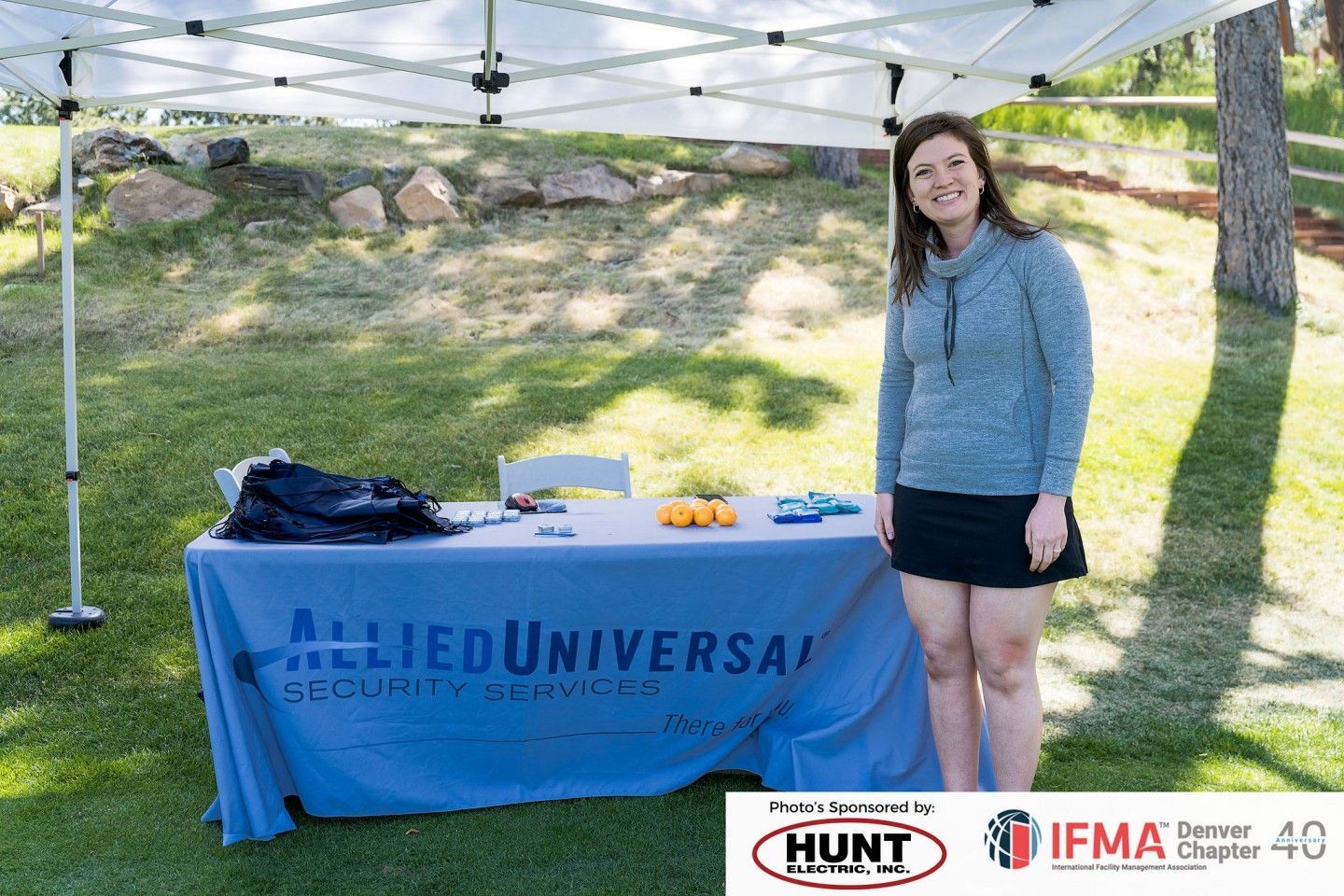 Woman standing by an Allied Universal Security Services booth at an outdoor event.