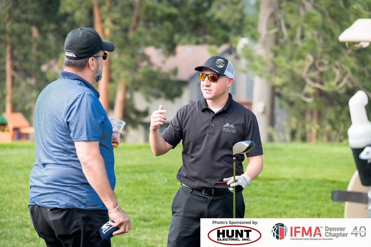 Two men talking on a golf course. One gestures while holding a golf club.