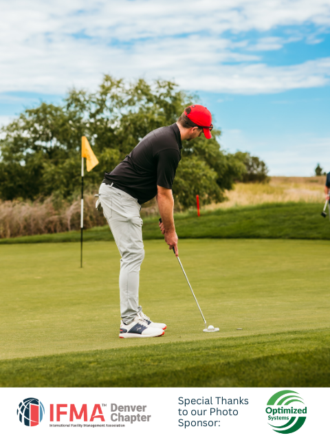 Man in black shirt and red hat putting golf ball on a green, flag in background.