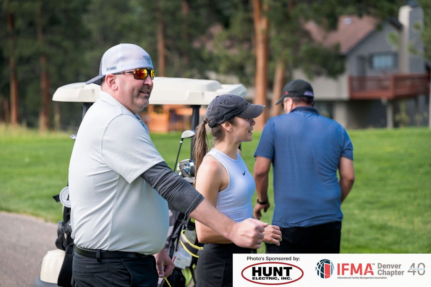 People on a golf course. Man in a cap smiles at another person next to a golf cart.