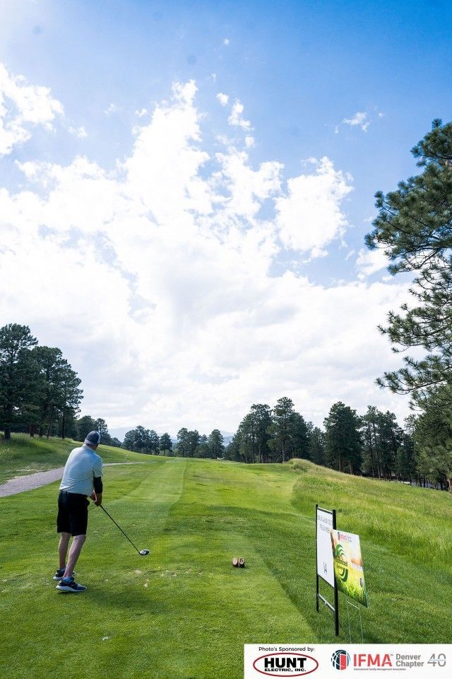 Golfer about to swing club on green golf course under a cloudy sky.