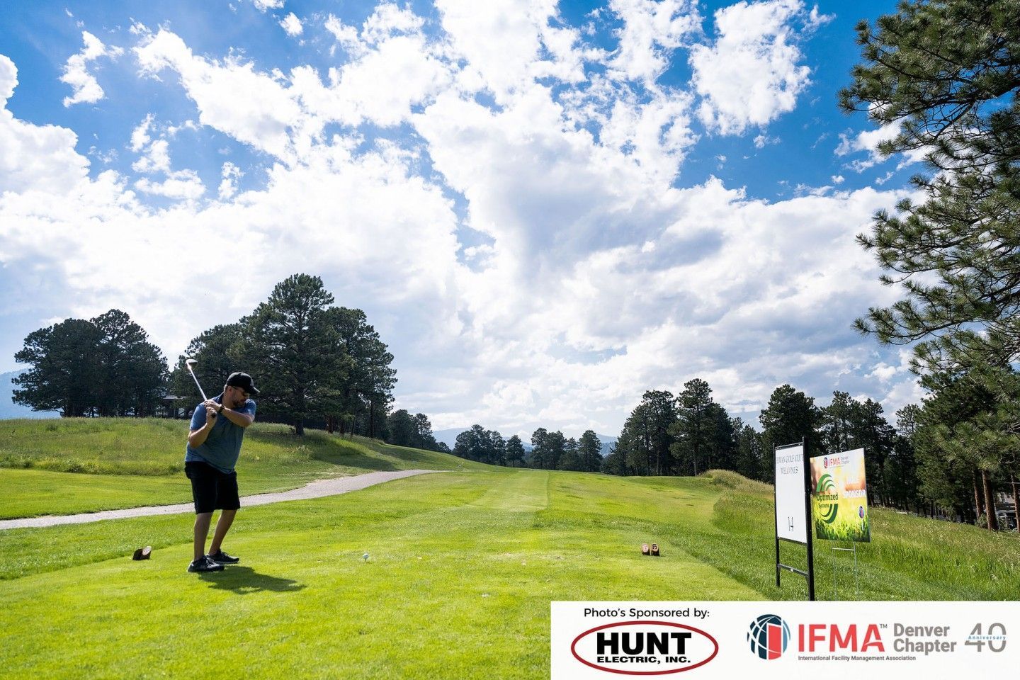 Golfer teeing off on a green golf course under a cloudy sky.