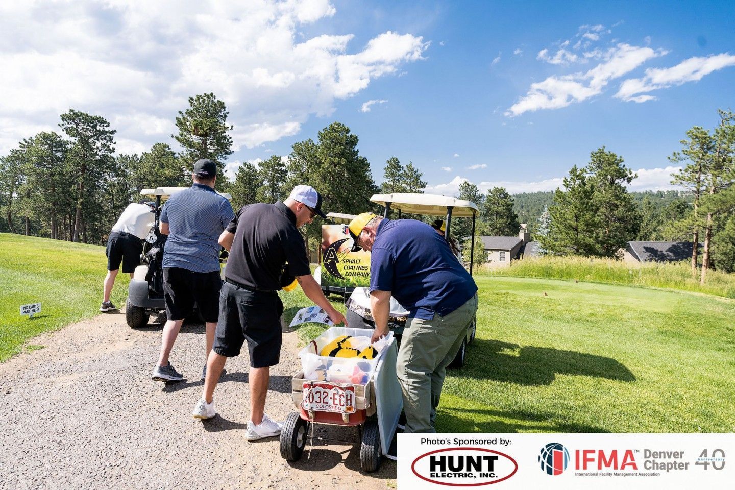 Golfers gather near golf carts on a course; one sorts items from a cart. Sunny day.