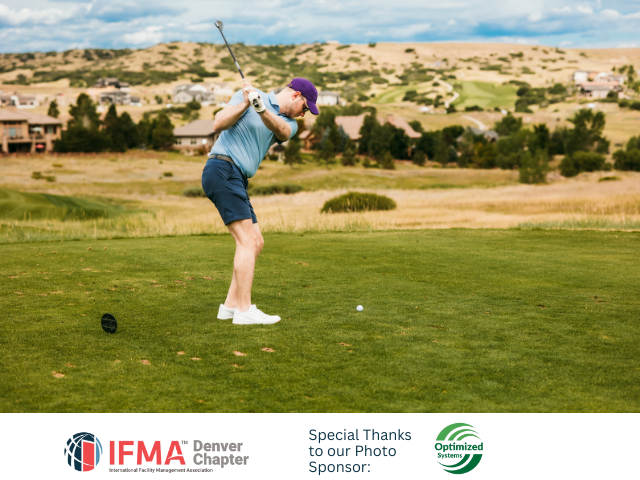 Golfer swinging club on green, preparing to hit the ball. Mountains and houses in the background.