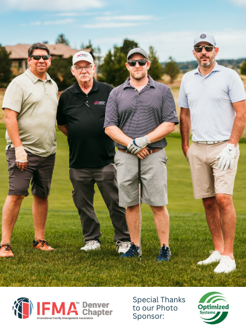 Four men on a golf course pose for a photo. They wear golf attire. Green grass and a blue sky are in the background.