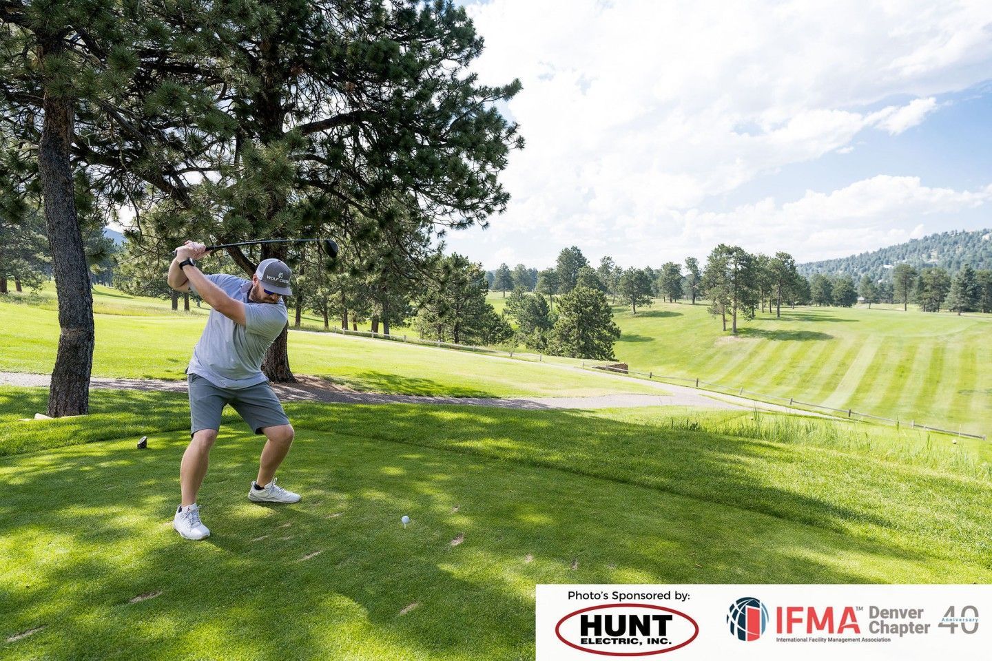 A person swings a golf club on a green course under a sunny sky.