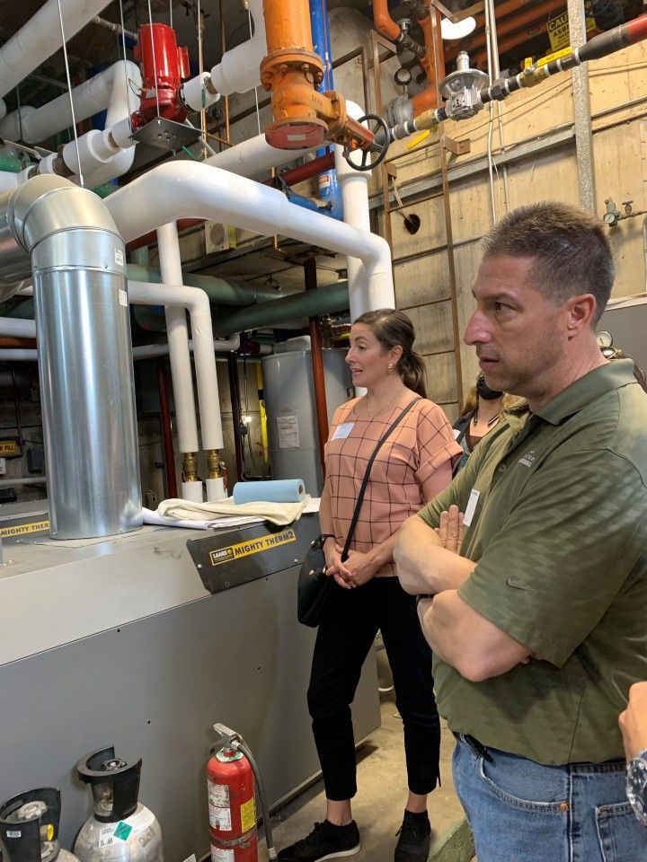 Two people looking at industrial equipment in a facility. Pipes and valves visible.