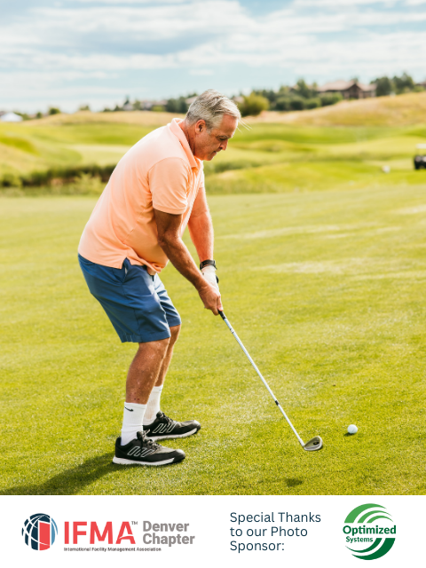 Man swinging golf club on a green course, orange shirt, blue shorts.