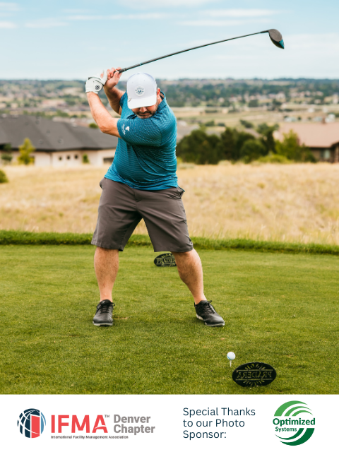 Man swinging a golf club on a green, ball teed up. Blue shirt, gray shorts, white hat. Landscape background.