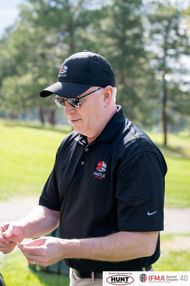 Man in black shirt and cap, holding something small outdoors; logo visible on shirt and cap.