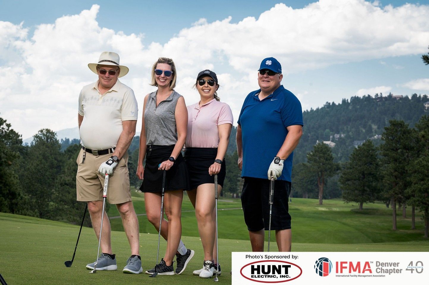 Four people with golf clubs on a golf course under a cloudy sky.