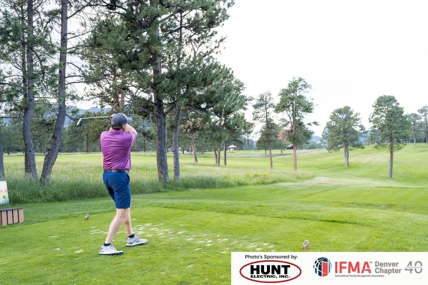 Person swinging a golf club on a green course, trees in the background. Sponsored logos at the bottom.