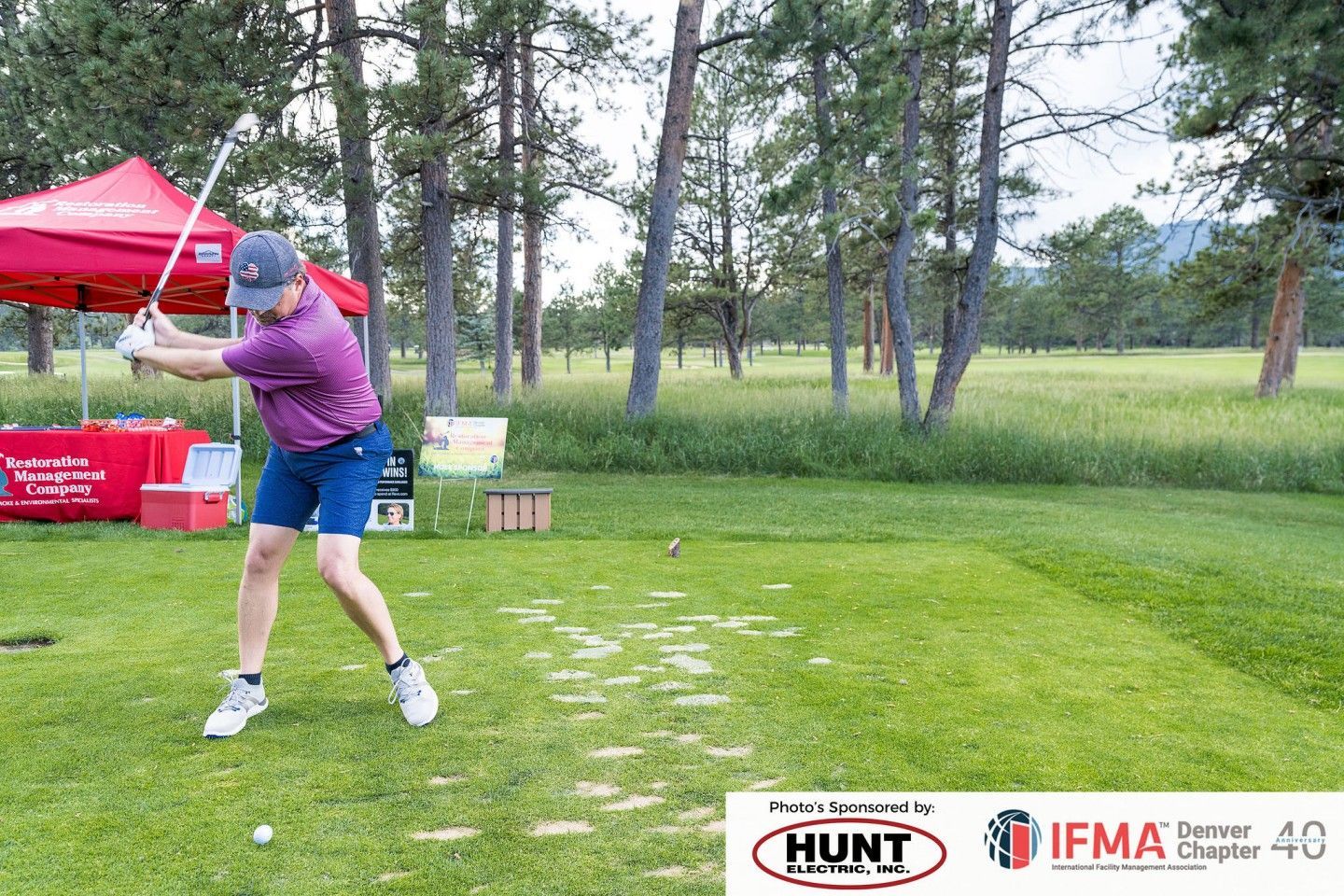 Golfer swings a club on a green course; red canopy in the background.