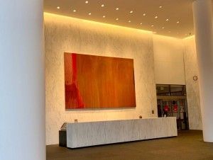 Lobby with large abstract painting above a reception desk. Warm-toned colors.