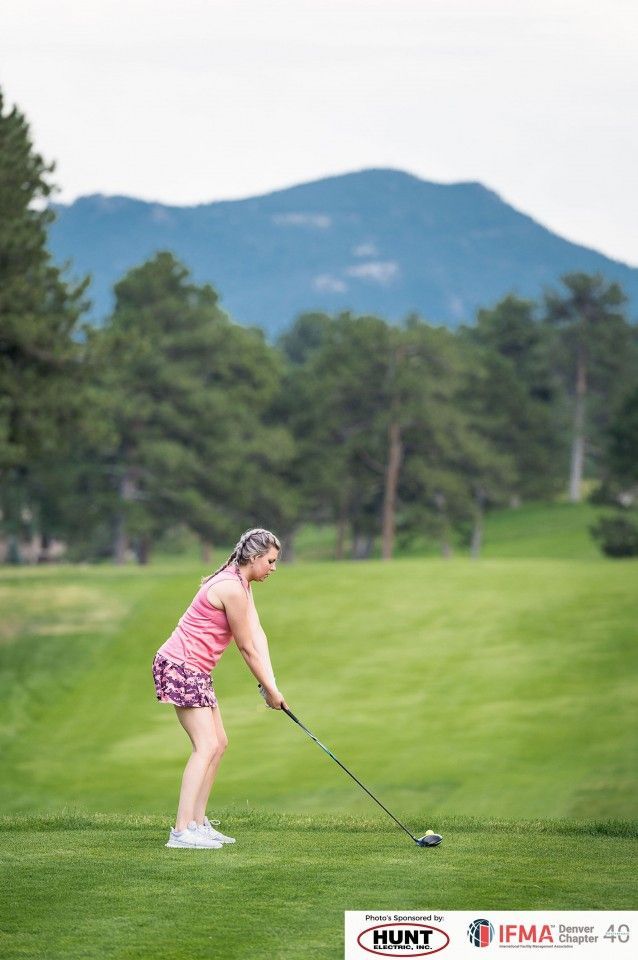 Woman golfing on a green course, mountain backdrop, about to swing.