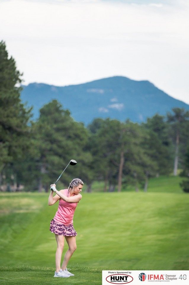Woman swinging a golf club on a green course, mountain backdrop.