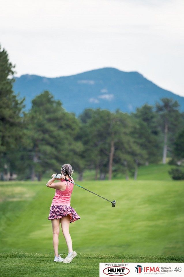 Golfer in pink swinging club on green course with mountain backdrop.