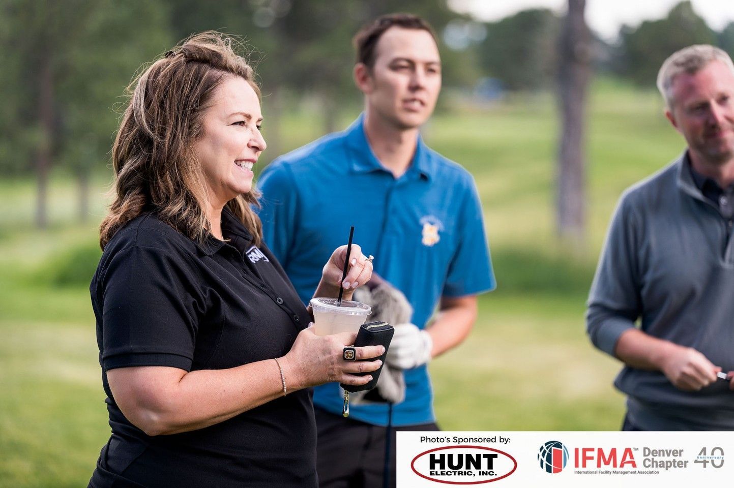 Woman holding drink and gesturing, with two men, on a golf course.