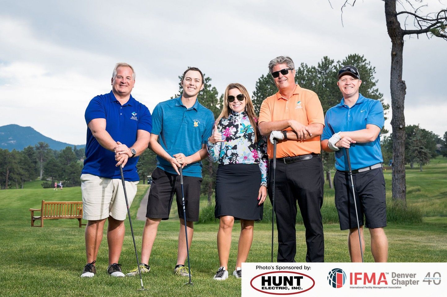 Five people with golf clubs on a course, posing for a photo.